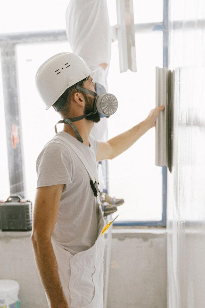 Handwerker verspachtelt eine Trockenbauwand mit Helm und Atemschutz
